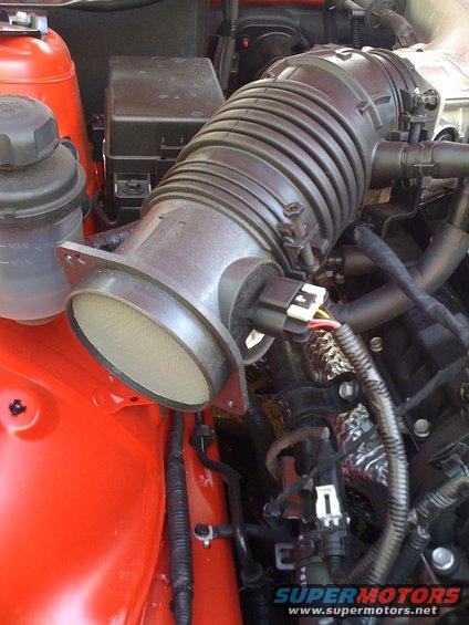 Orange engine bay with black air intake tube and filter housing. Supermotors.net logo visible