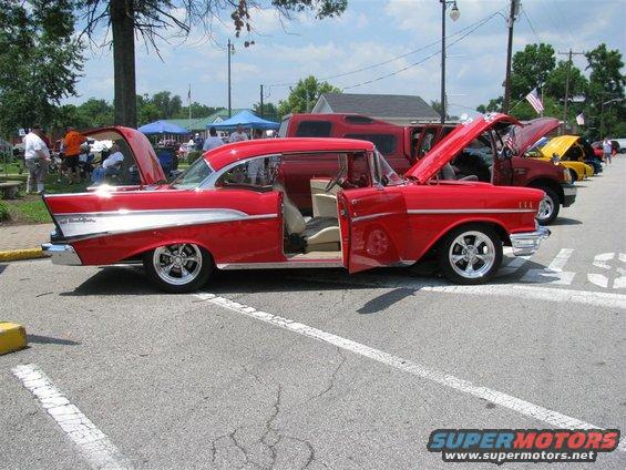 Red 1957 Chevrolet Bel Air coupe with doors and hood open, chrome trim, and custom wheels