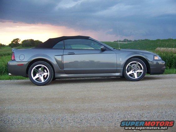 Gray Ford Mustang convertible parked on a dirt road with a cloudy sky