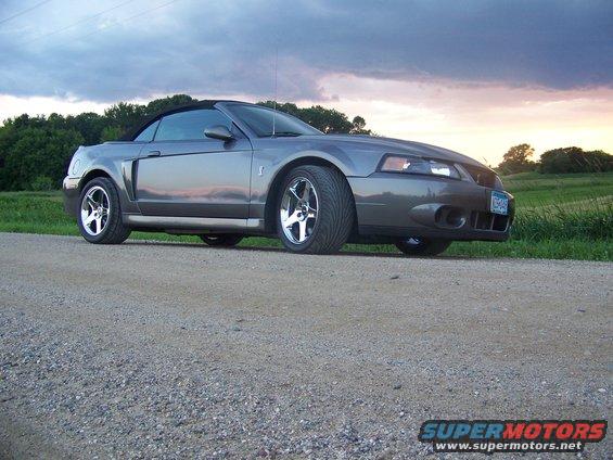 Gray Ford Mustang convertible with a black top parked on a gravel road