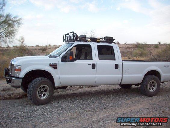 White four-door pickup truck with a roof rack carrying tools, viewed from the side