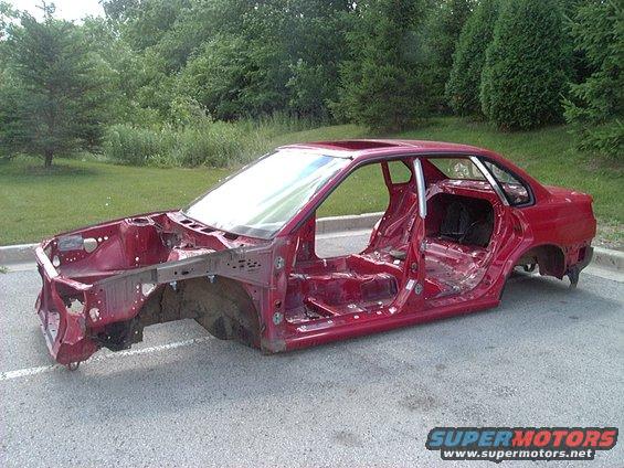 Red 1997 Subaru Legacy sedan body shell, stripped of all panels and interior, parked outdoors