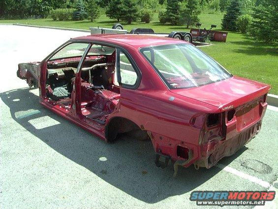Red car body shell, stripped down to the metal, parked outside. Doors and hood are open