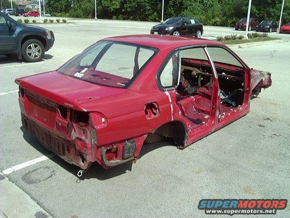 1997 Subaru Legacy shell, red, stripped down to the frame, parked in a lot