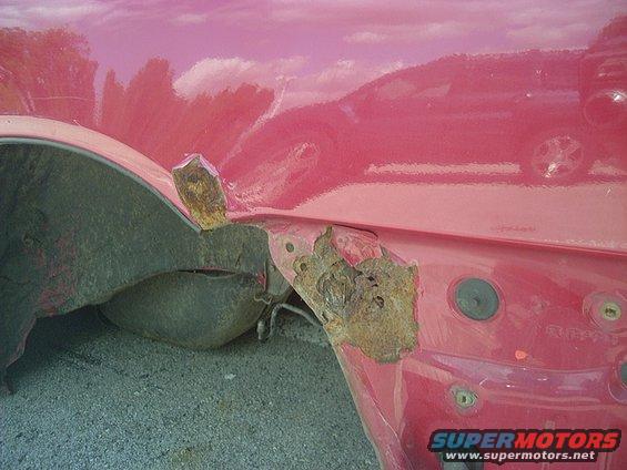 Red car fender with significant rust around the wheel well and mounting points