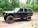 1994 Ford F-250 - Modified black Jeep Cherokee with off-road tires and custom bumper sits on a dirt trail.