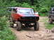 1994 Ford F-250 - A lifted red Ford pickup truck navigates a dirt trail in a wooded area, accompanied by other off-road vehicles.