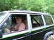 1994 Ford F-250 - A man smiles from the driver's seat of a black Jeep Cherokee XJ with a green stripe, seen off-road.