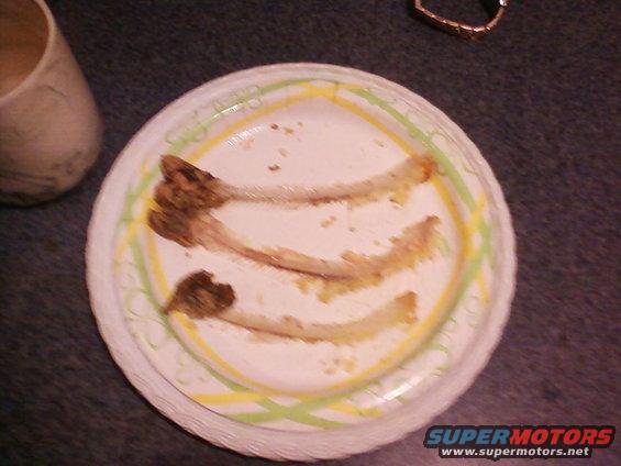 Paper plate with three fish bones and crumbs, next to a cup
