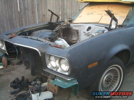 Car front end with hood open, engine removed, parts scattered around. Looks like a 1973 Ford Ranchero