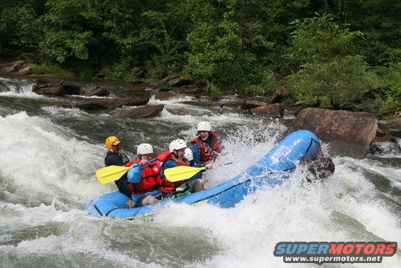 People whitewater rafting down a rocky river with trees in the background. Water splash