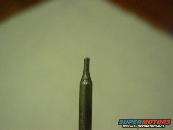 Close-up of a metal tool bit with a pointed tip against a plain background. Supermotors.net logo in lower right