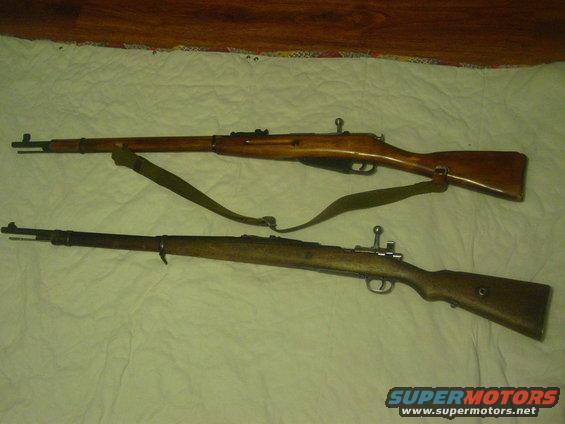 Two rifles laid out on a white surface. One is lighter wood, the other darker