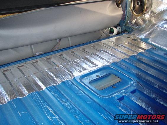Sound deadening material applied to the blue metal floor of a vehicle interior, with a speaker visible in the upper right