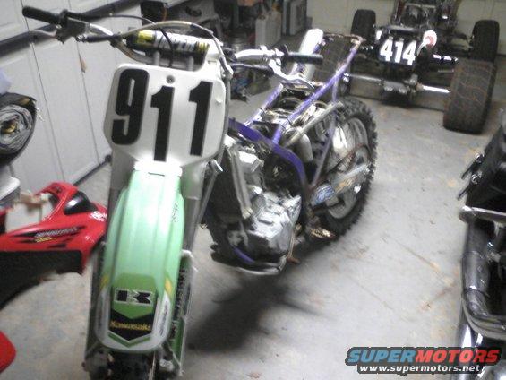 Dirt bike with number 911 on front plate, partially disassembled. Another vehicle with number 414 visible in background