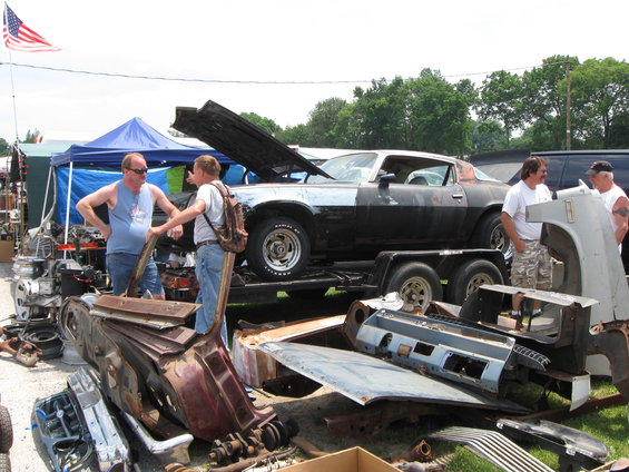 Black and silver muscle car on trailer, hood open, with car parts scattered around