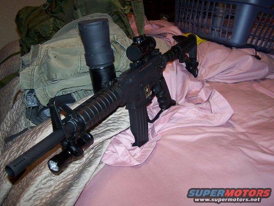 Black assault rifle with scope and flashlight mounted on barrel, resting on pink bedding