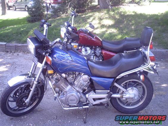 Two motorcycles parked outdoors, one blue with flames, one red. Text 'SUPERMOTORS' visible