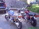1982 Yamaha Virago - Two motorcycles are parked side-by-side in front of a wooden fence, with a pickup truck and another vehicle in the background.