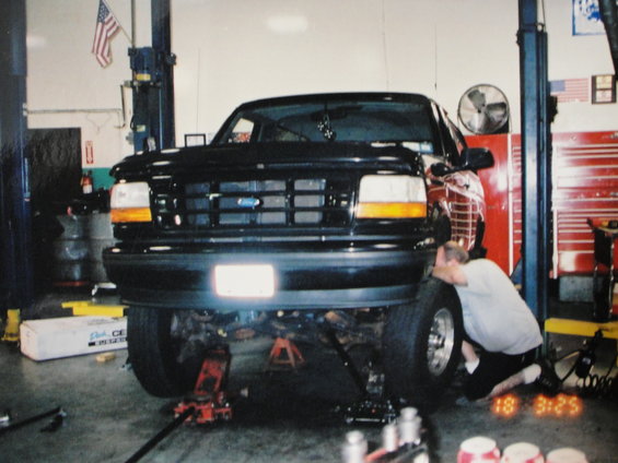 Black Ford Bronco on car lifts, front view. Mechanic works on front wheel