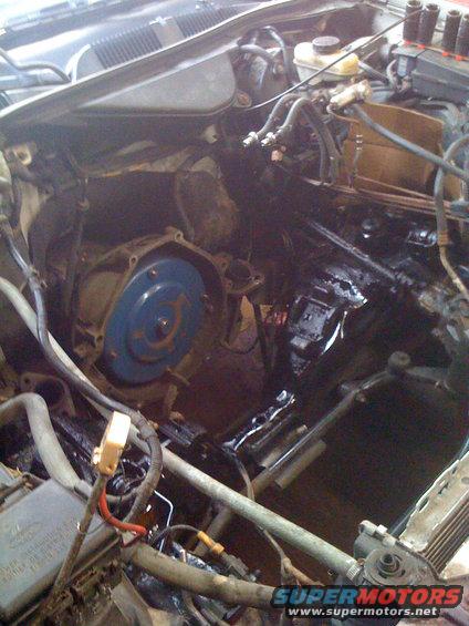 Engine bay showing transmission bell housing and torque converter, with various hoses and wiring
