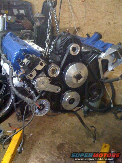 Engine assembly with blue valve covers and chrome pulleys being lifted by a chain