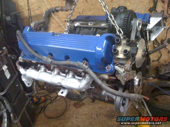 Blue engine assembly with silver exhaust manifolds, suspended by chains