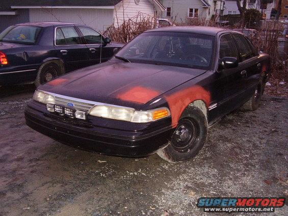 Black Ford Crown Victoria with red primer on fender and hood, parked next to another dark sedan