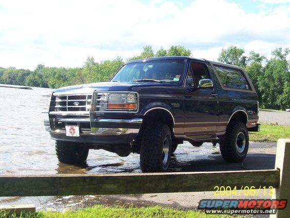 Dark blue Ford Bronco with tan trim, lifted, partially submerged in water, front 3/4 view