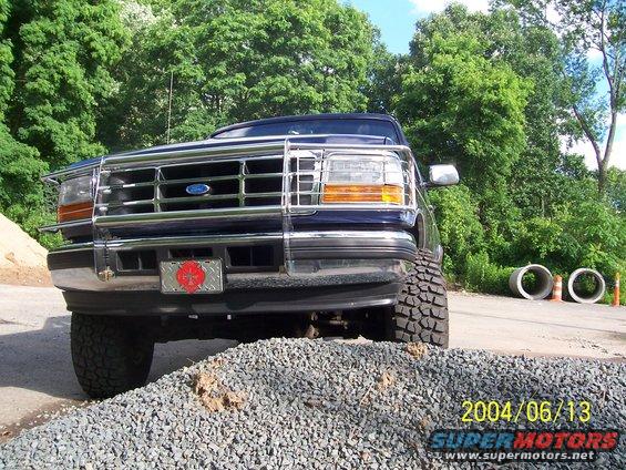 Front view of a dark blue Ford Bronco with a chrome bull bar and large tires, parked on gravel
