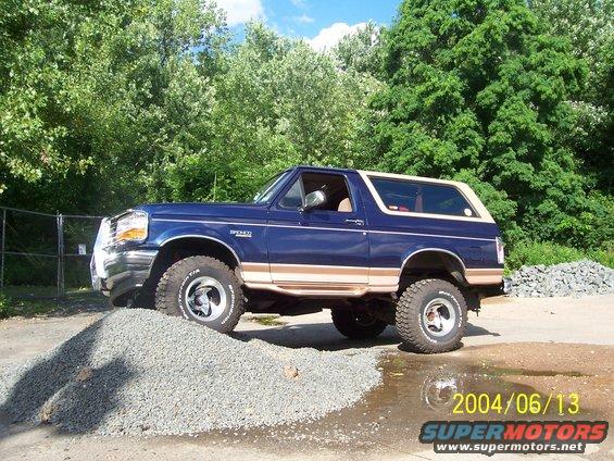 Blue Ford Bronco with tan trim, lifted, driving over gravel pile