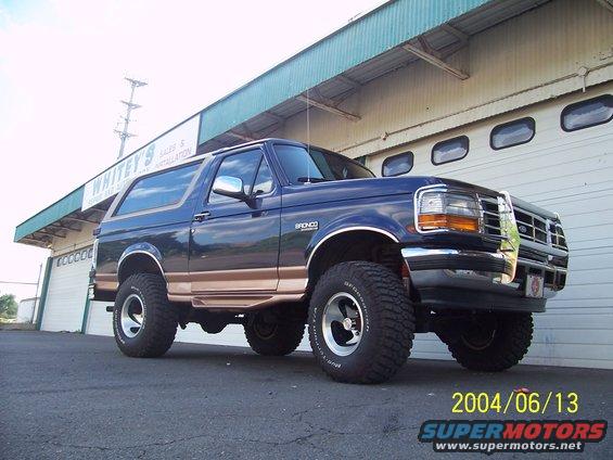1990 Ford Bronco, dark blue with tan trim, lifted with aftermarket wheels and tires, parked in front of a garage