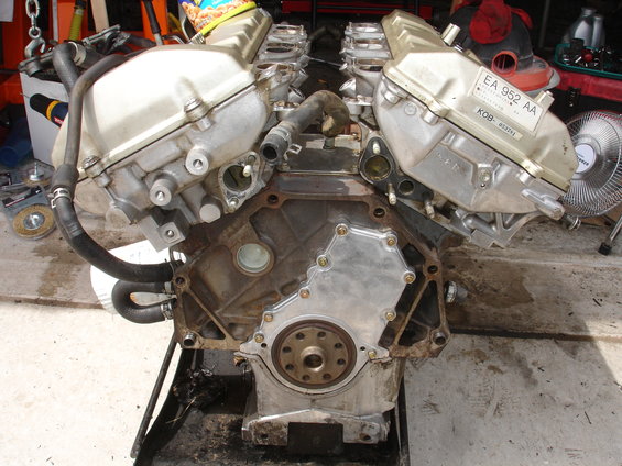 Engine block with aluminum valve covers and hoses attached, resting on a stand