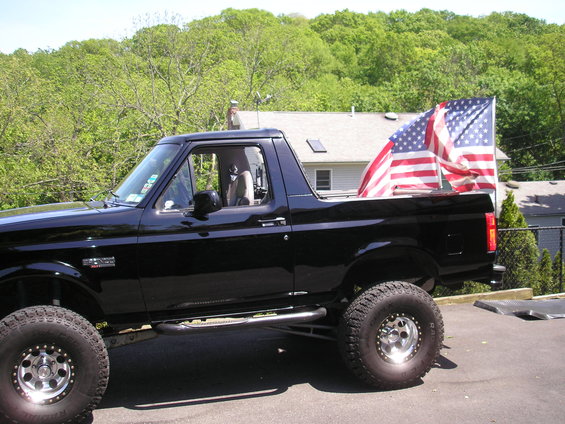 Black 1995 Ford Bronco with American flags in the bed, parked outside