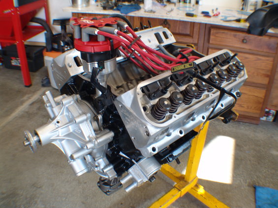Engine on yellow stand, silver water pump, red distributor cap, black engine block, silver valve covers