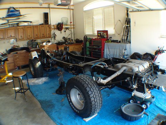 Vehicle chassis on blue tarp in garage, undergoing engine rebuild