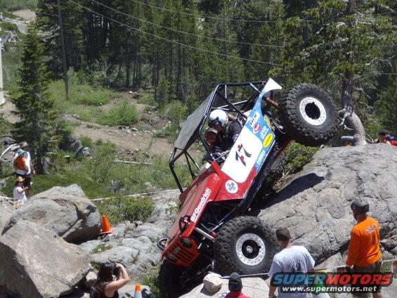 Red off-road vehicle with a roll cage climbing over rocks, BFGoodrich tires visible