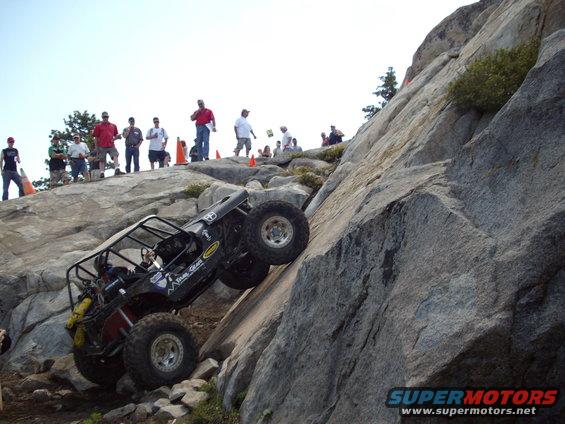 Off-road vehicle climbing steep rock face with spectators watching