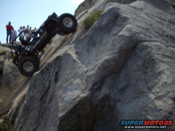 Off-road vehicle on a steep rock face with spectators watching