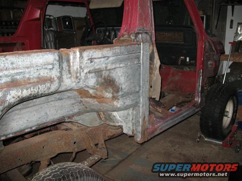 red truck body, missing panels, showing rust and damage. Interior visible