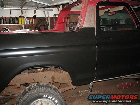 Black and red 1978 Ford Bronco, side view, showing rust on the frame and a partially painted body