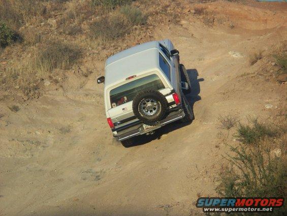White 1996 Ford Bronco driving on a dirt trail, rear view
