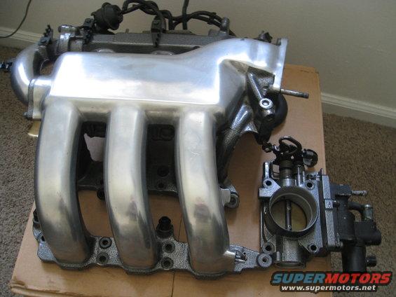 Polished aluminum intake manifold and black throttle body on a cardboard surface