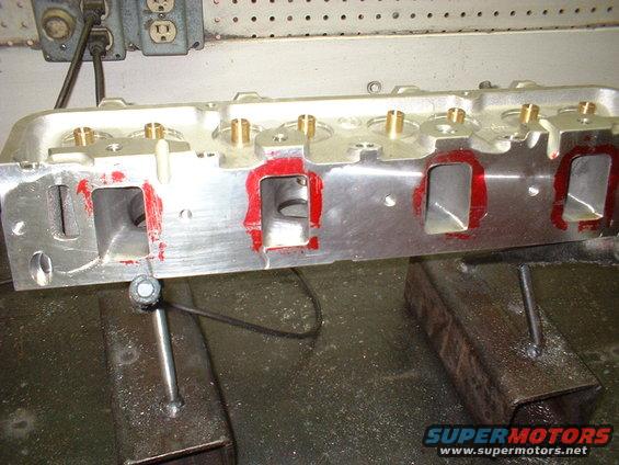Aluminum engine cylinder head with red sealant around ports, mounted on a workbench