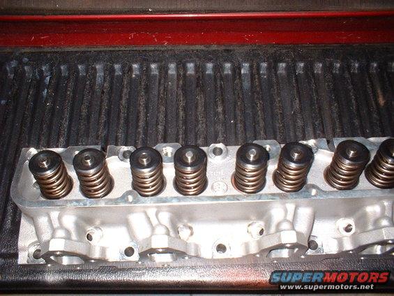 Aluminum engine cylinder head with valve springs visible, resting on a ribbed surface