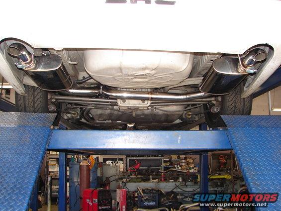 Underside of a car showing a dual-tip aftermarket exhaust system and fuel tank