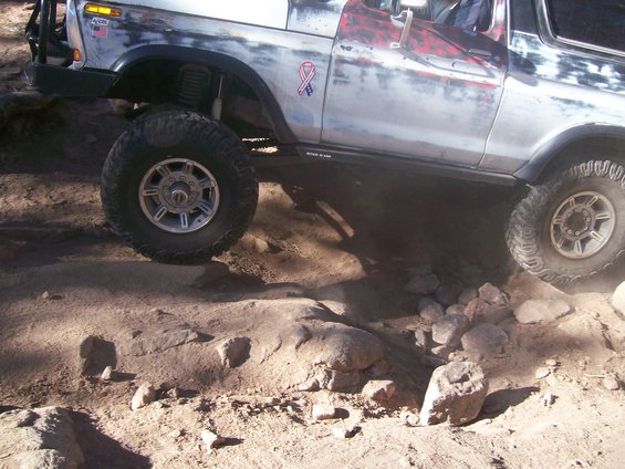 1978 Ford Bronco off-roading on rocky terrain, silver body with red accents, lifted suspension