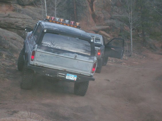 Gray 1978 Ford Bronco with "Dick CEPEK" sticker on rear window, off-road lights on roof, parked on dirt road