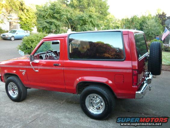 Red 1985 Ford Bronco II parked on driveway, side view with spare tire mounted on rear door