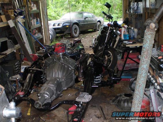 Black 1977 Pontiac Firebird in garage with engine and motorcycle parts